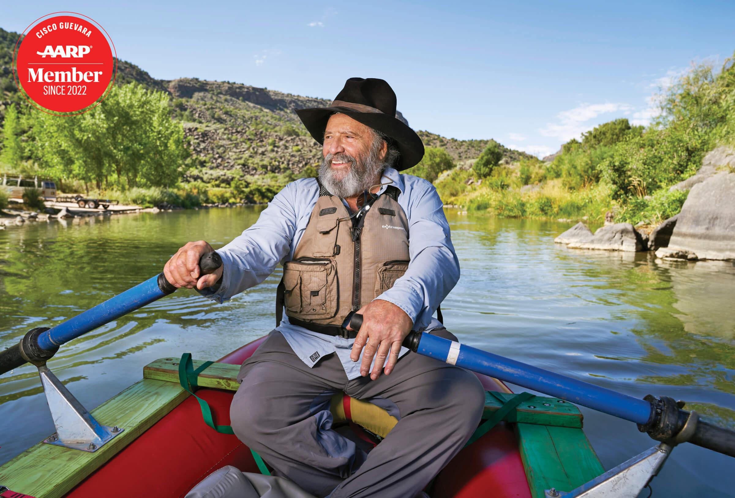 Image of an older man smiling and rowing a boat, wearing a brown vest