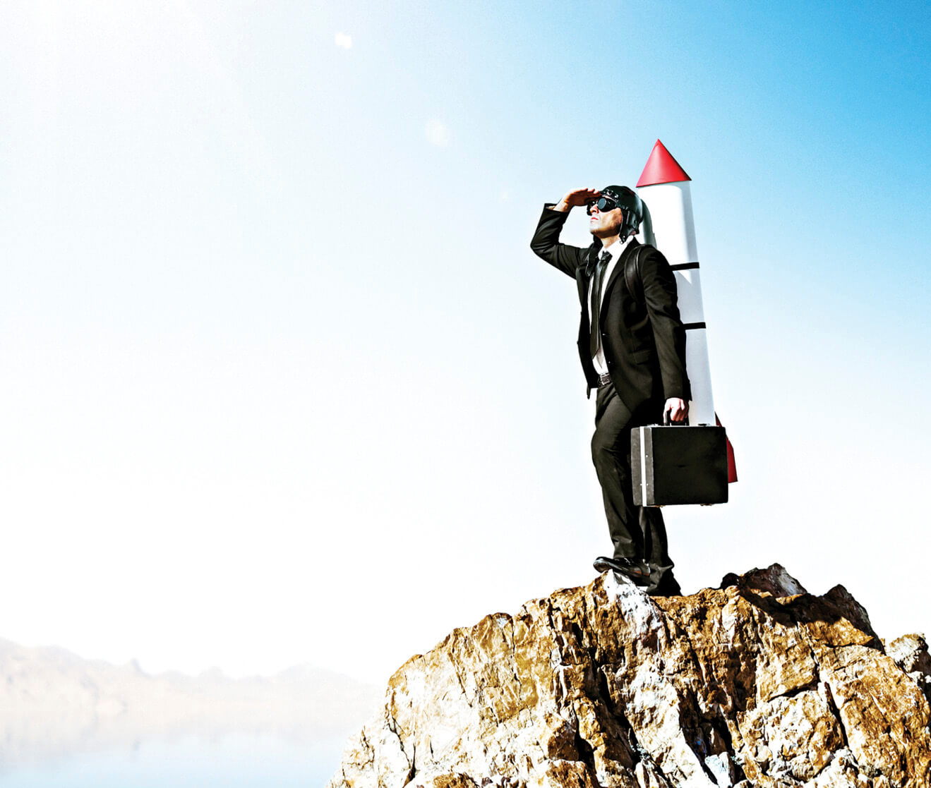 Image of a person standing on rock with a rocket strapped to his back&nbsp;