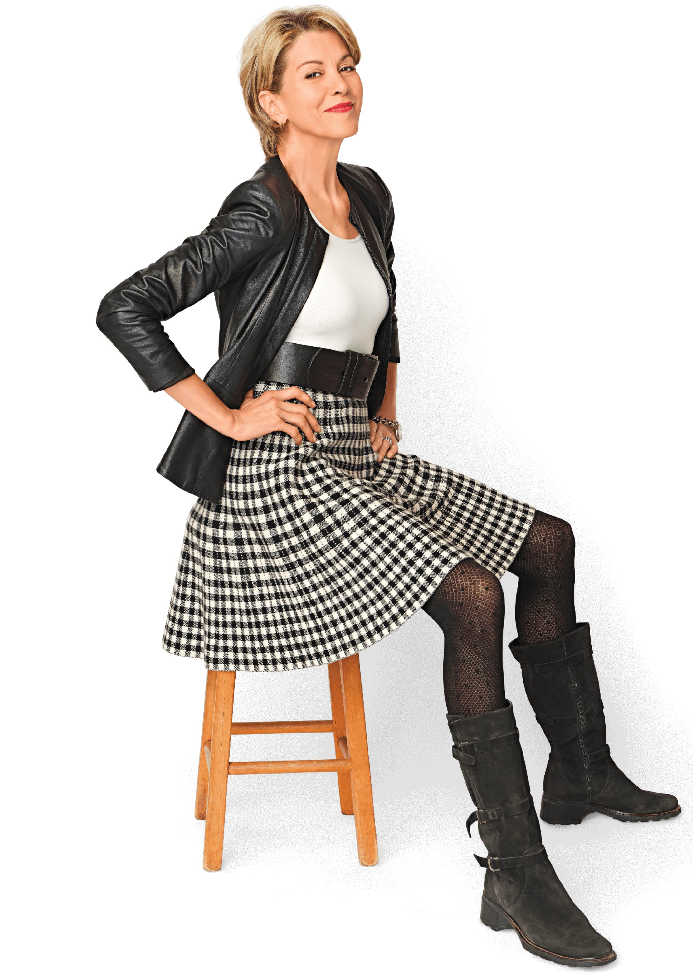 Image of Wendie Malik sitting on a wooden stool. She is wearing a leather jacket and a black and white checked skirt with black boots