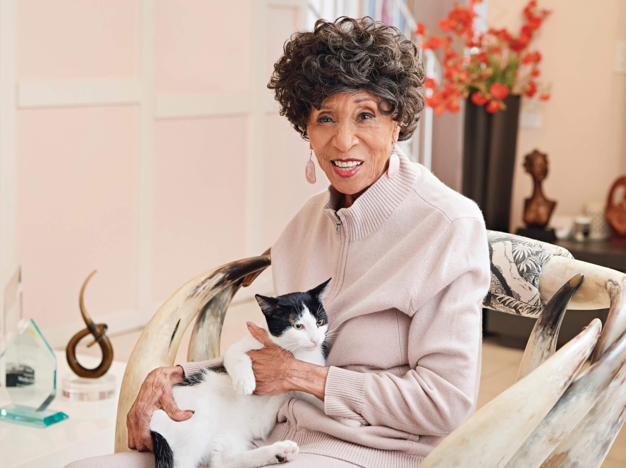 Photograph of Marla Gibbs wearing a light pink sweater and holding a tuxedo cat in her lap.&nbsp;