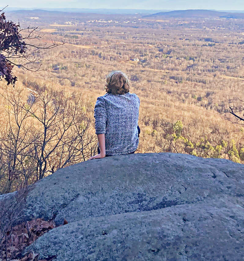 Photo of Aileen's son sitting at top of hike, overlooking landscape below.