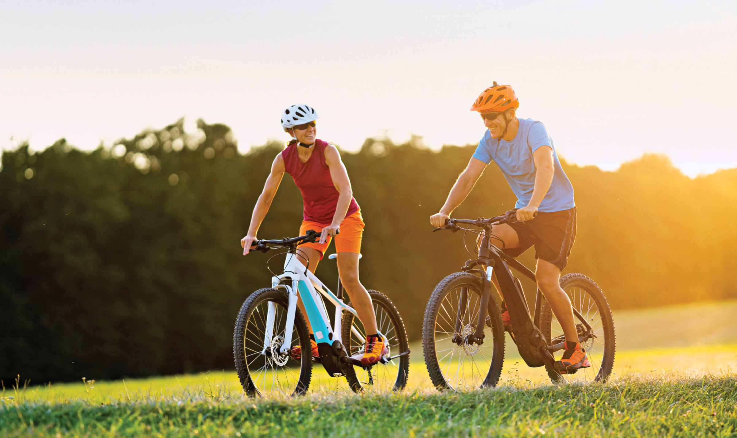 Photo of woman and man riding electric bikes on a grassy path