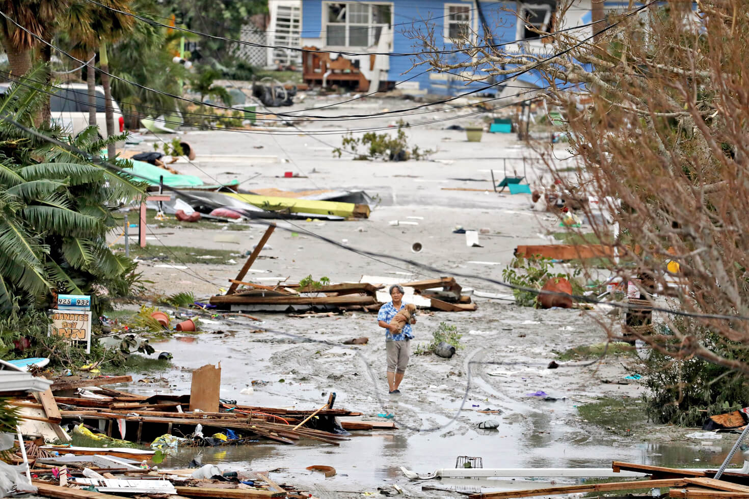 Photograph of a man standing in flood water holding his dog. They are surrounded by debris from hurricane damage.