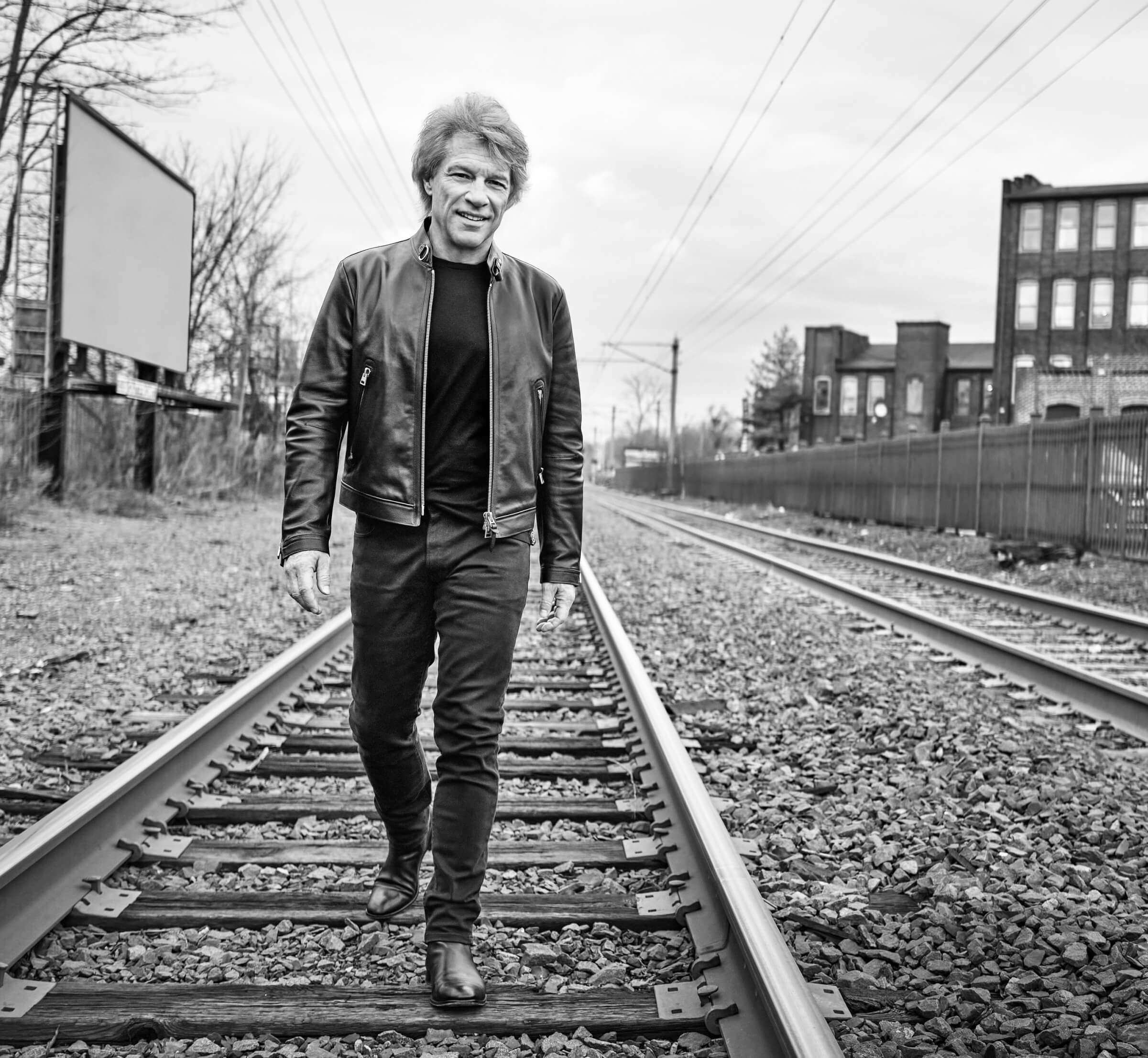 Black and white photo of Jon Bon Jovi walking along train tracks near his New Jersey home