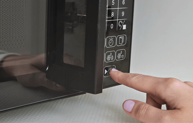 Photo of a hand pressing a button on a microwave