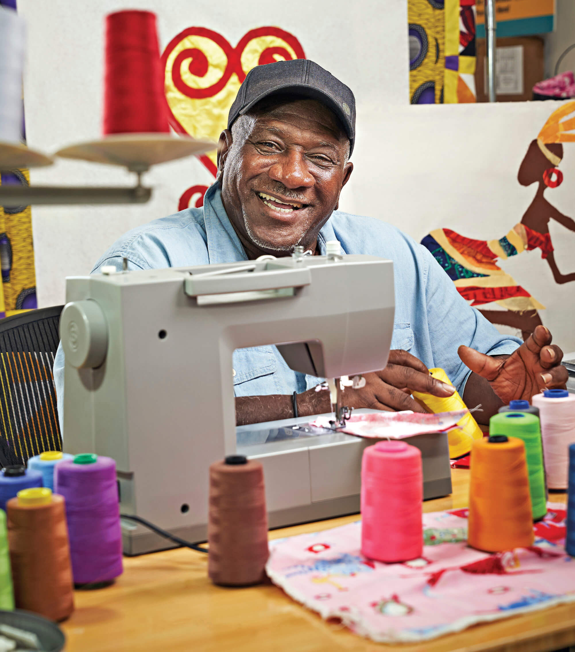 Gary Tyler sitting at a table with a sewing machine in front of him and smiling at the camera 