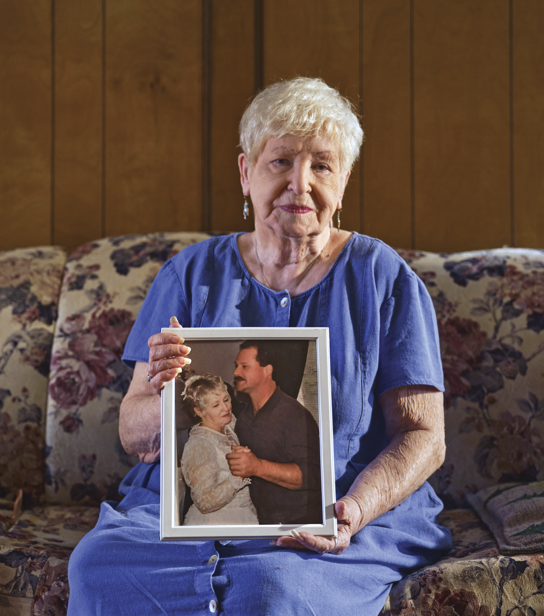 Photograph of Joanne Reed sitting on a couch and holding up a picture of her dancing with her son 