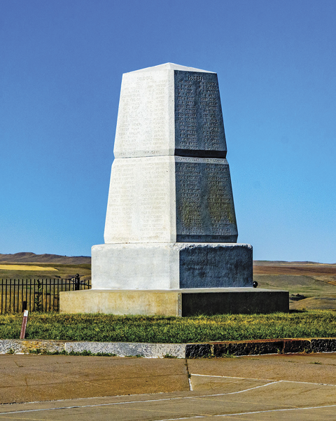 A big white marble headstone standing in the middle of the prairie against the blue sky 