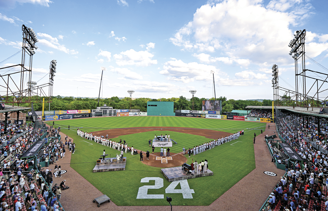 A baseball field with the number 24 written on the field. The stadium is full and the players are standing in formation on the field 