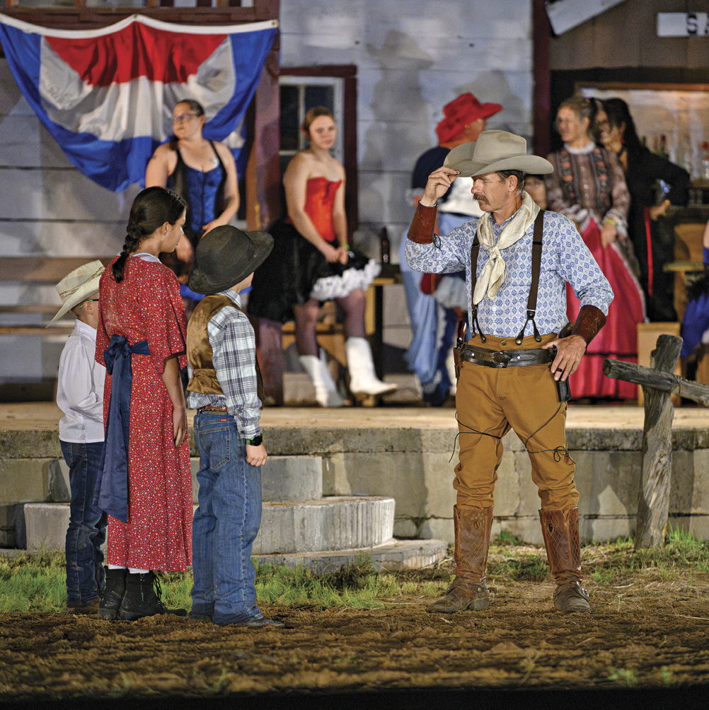 A group of performers in Western frontier-style clothing engages with children during the Old Lincoln Days reenactment event in New Mexico.