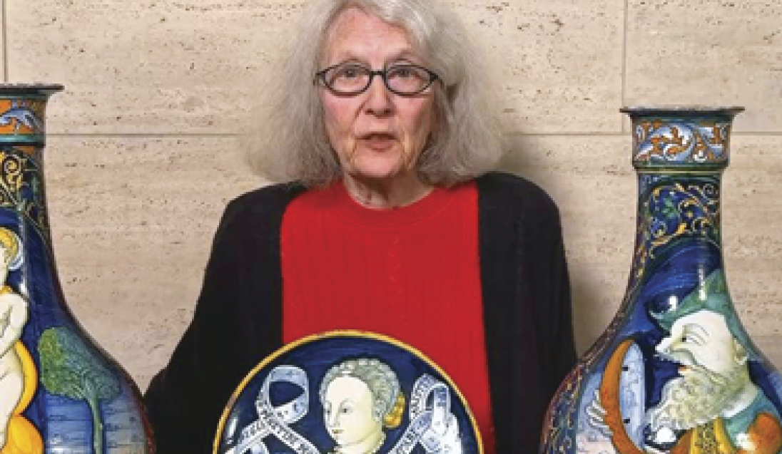Photograph of Alison Luchs in front of colorful ceramic vases 