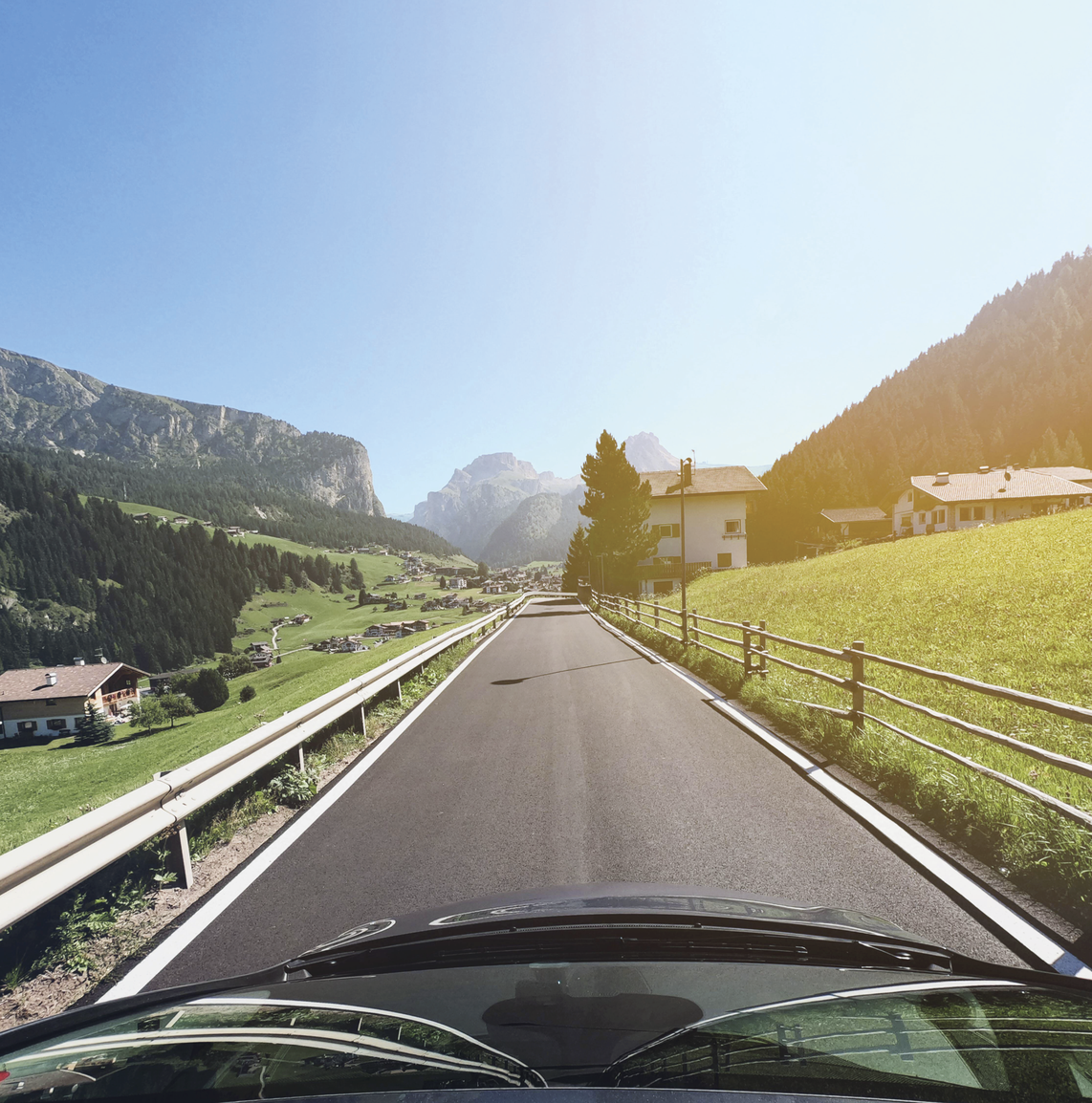 Photograph of a car driving down a road surrounded by fields of grass
