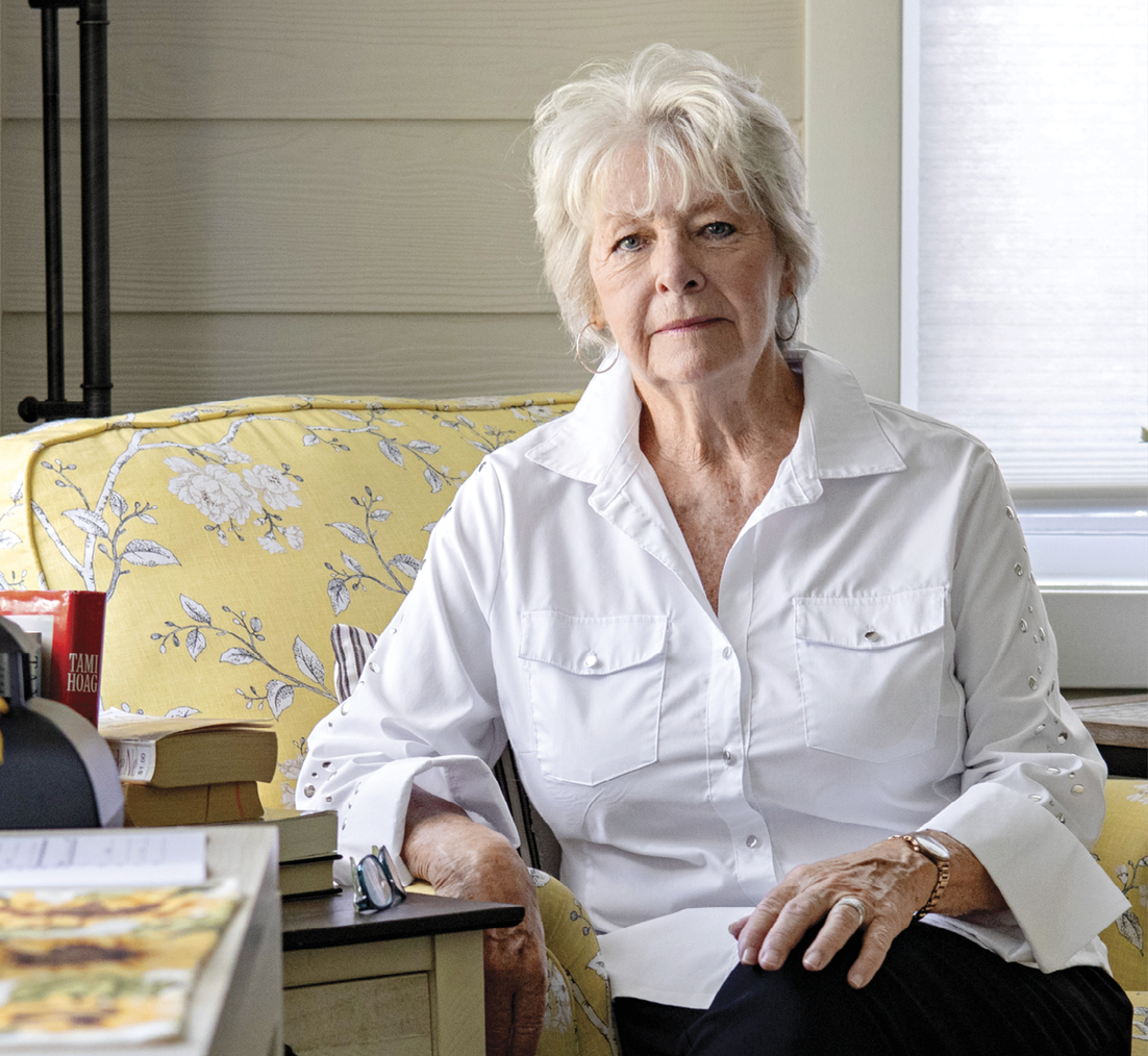 Portrait of Spath wearing a white shirt and sitting on a floral chair 