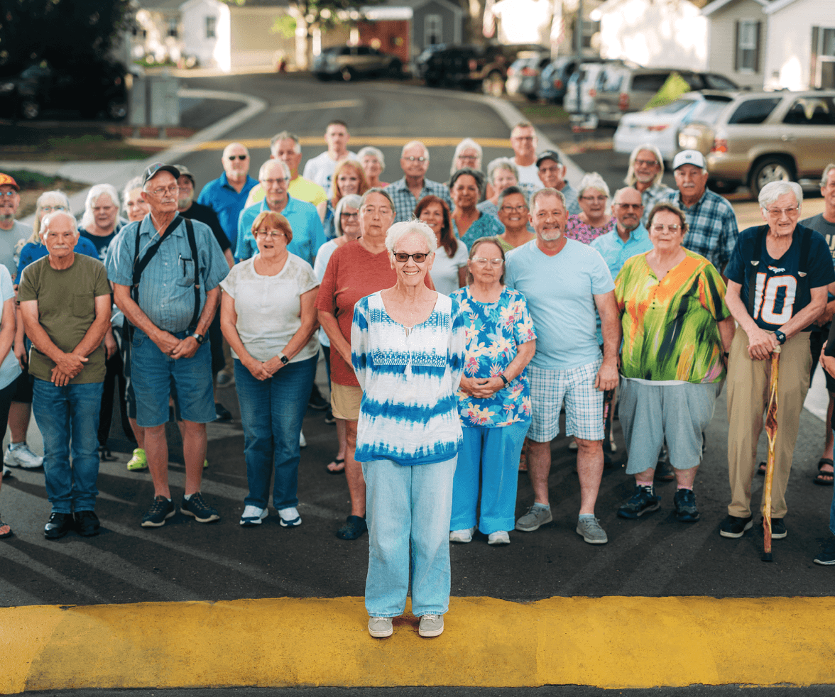 Photograph of the residents of Meadowood Village all standing behind the Sandy Cook in the middle of the street 