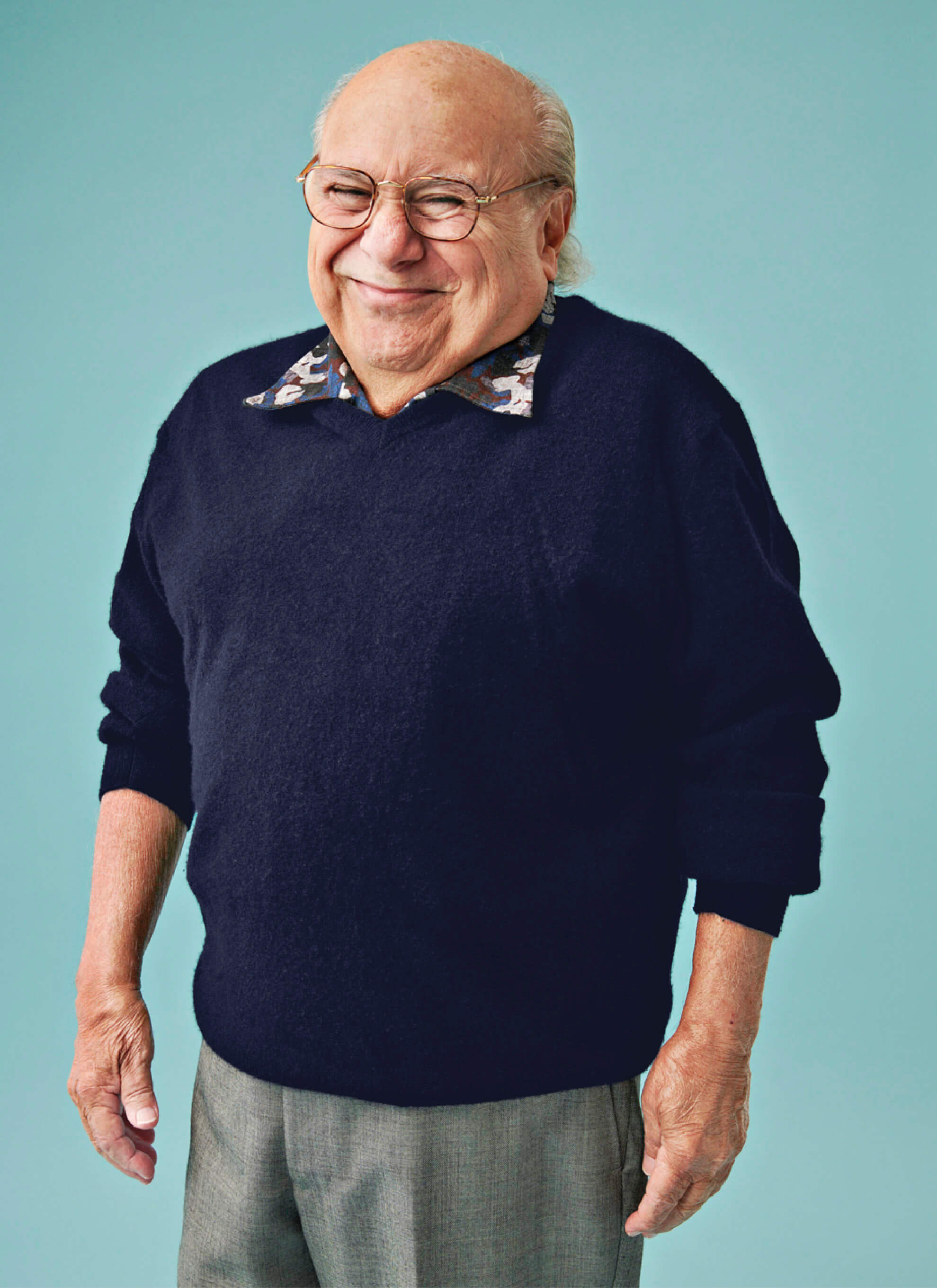 Portrait of Danny DeVito wearing a dark blue sweater and grey pants