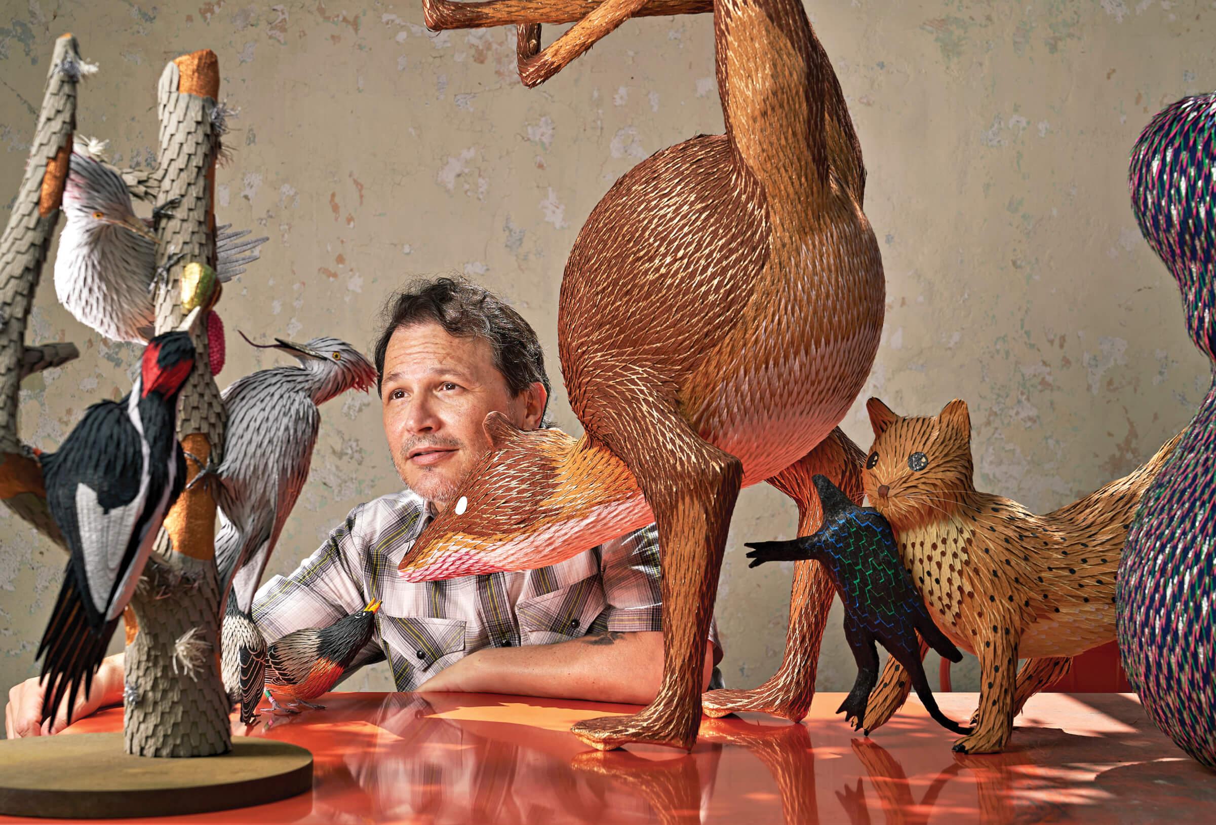 Photograph of Roberto Benavidez sitting at a table surrounded by his art 