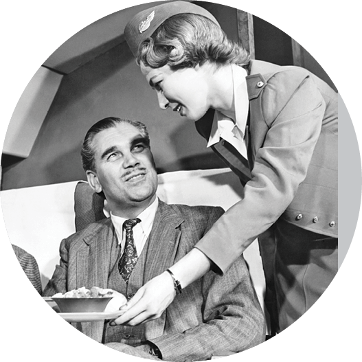 Black-and-white vintage photo of a stewardess serving a male passenger on an airplane