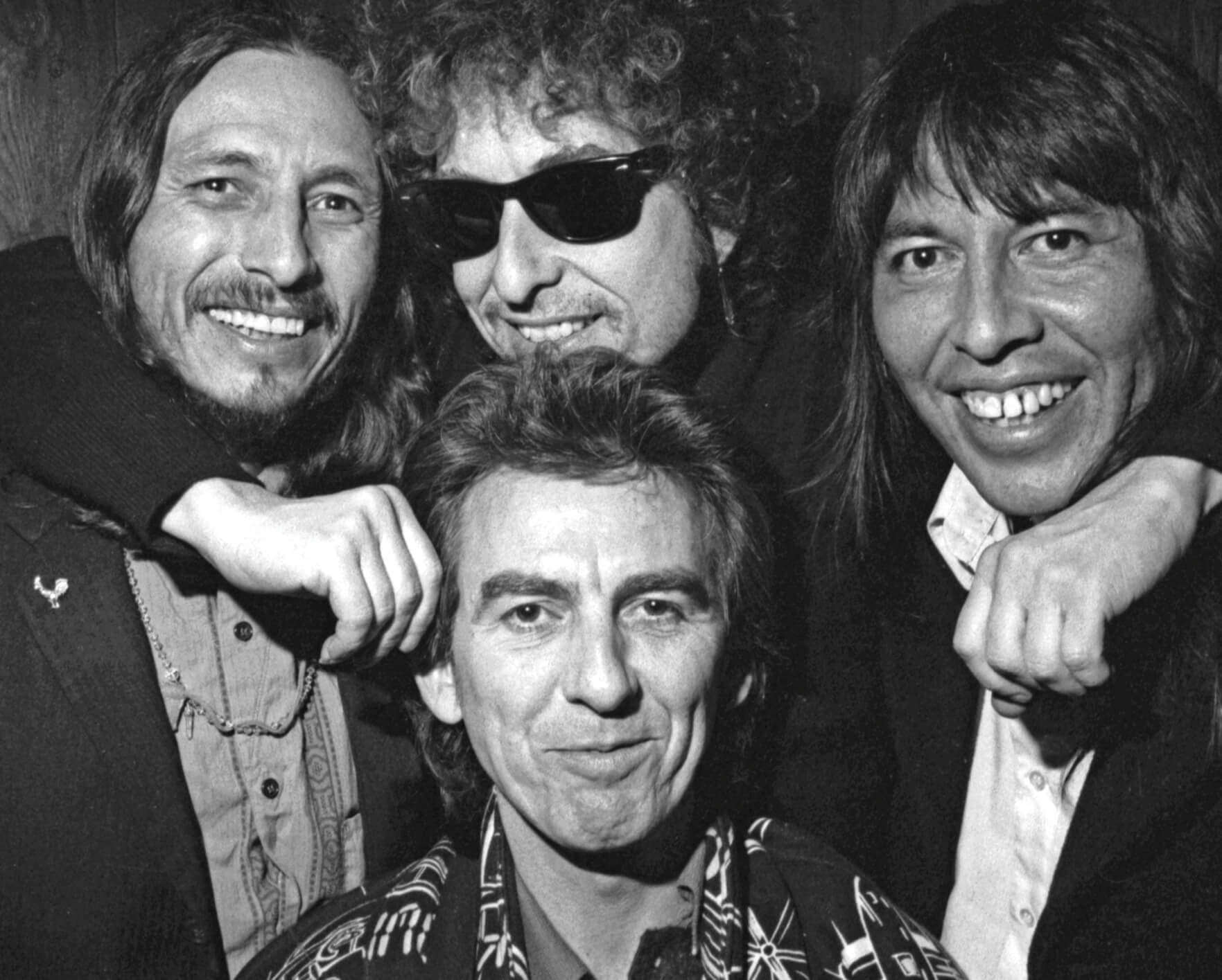 Black-and-white photo of a smiling Bob Dylan with John Trudell, George Harrison and Jesse Ed Davis in 1987