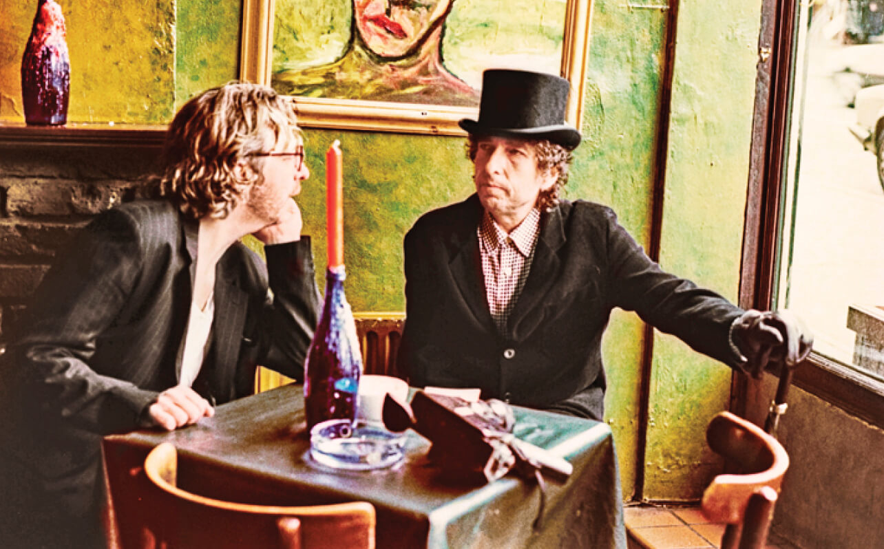 Photo of Dave Stewart sitting at a table with Boby Dylan in the early 1990s
