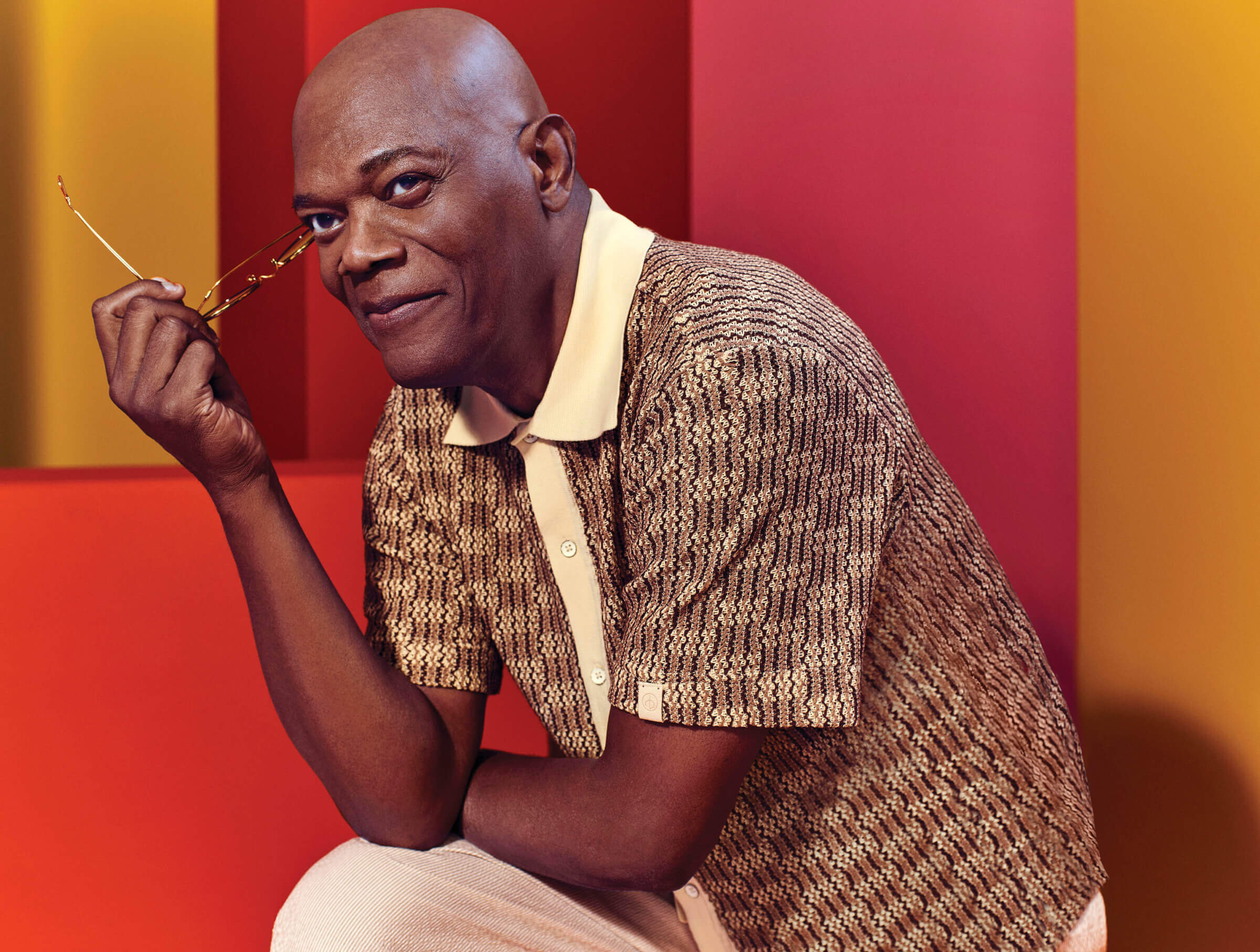 Photo of Samuel L. Jackson in a brown and cream shirt, smiling and holding his glasses in one hand