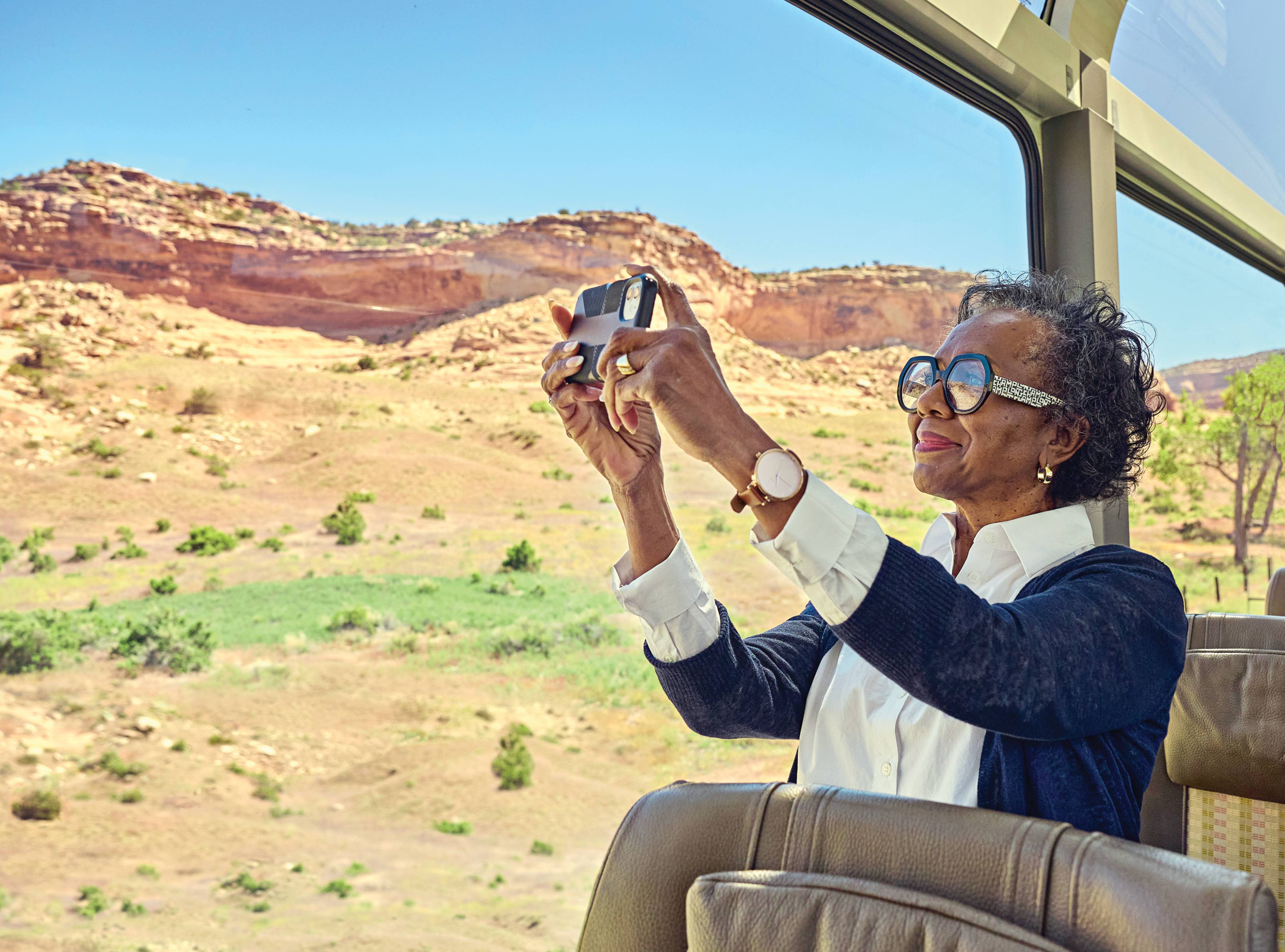 Photograph of an older woman taking a photo on her phone of the mountains