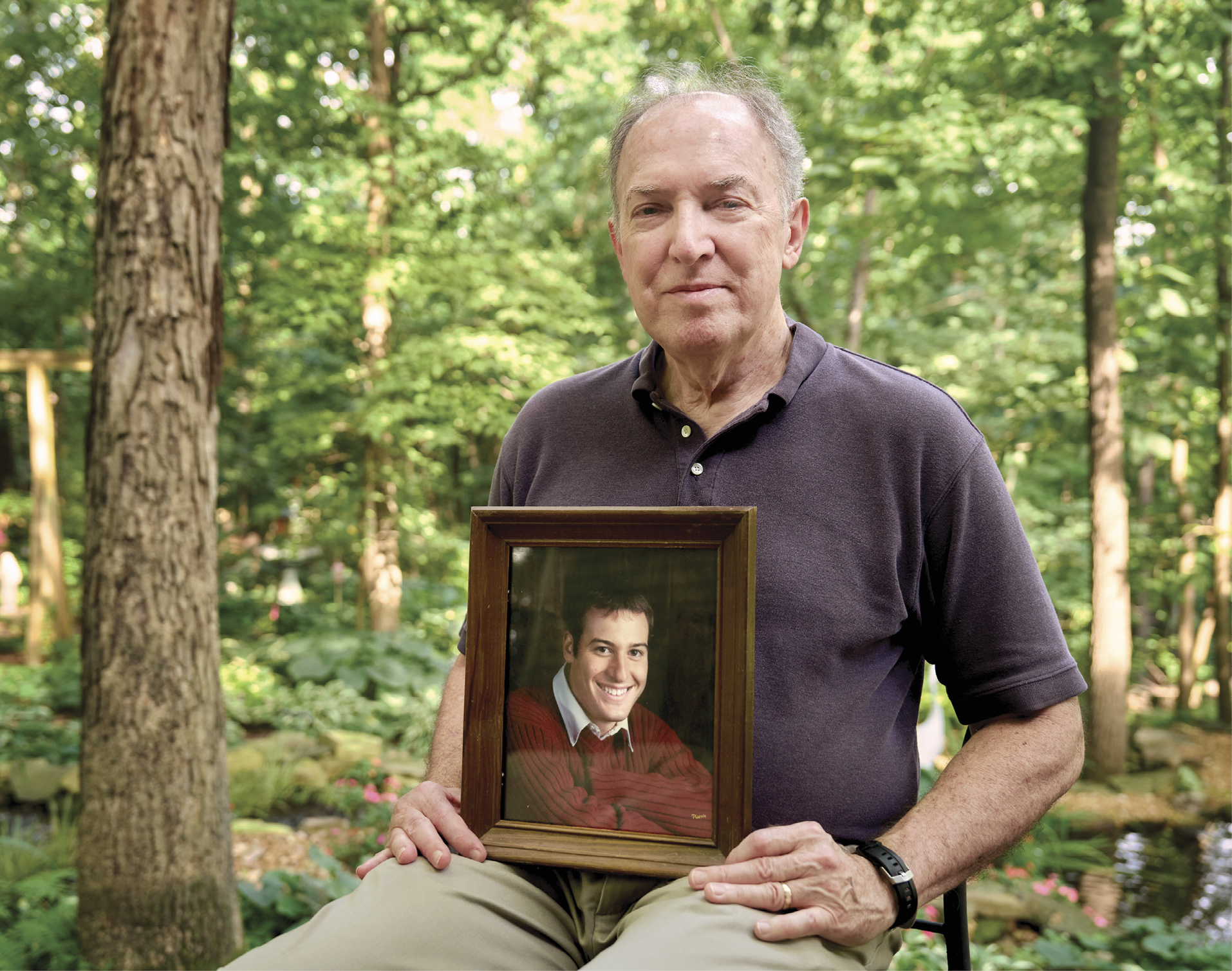 Larry McCord sitting in a forest holding up a framed picture of his son