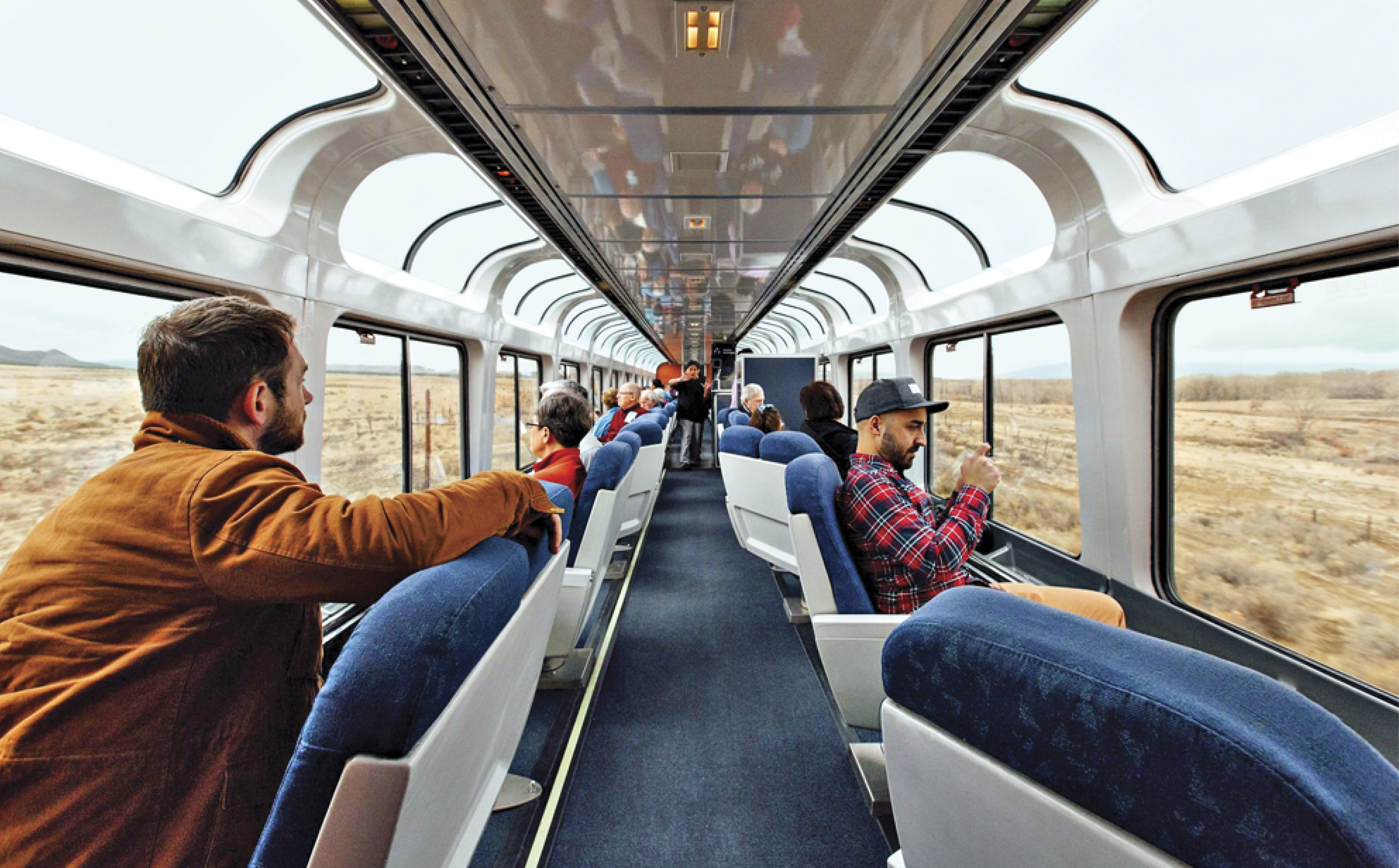 Image of the inside of train with several people taking pictures of the view outside. The train has window on the ceiling and on the sides