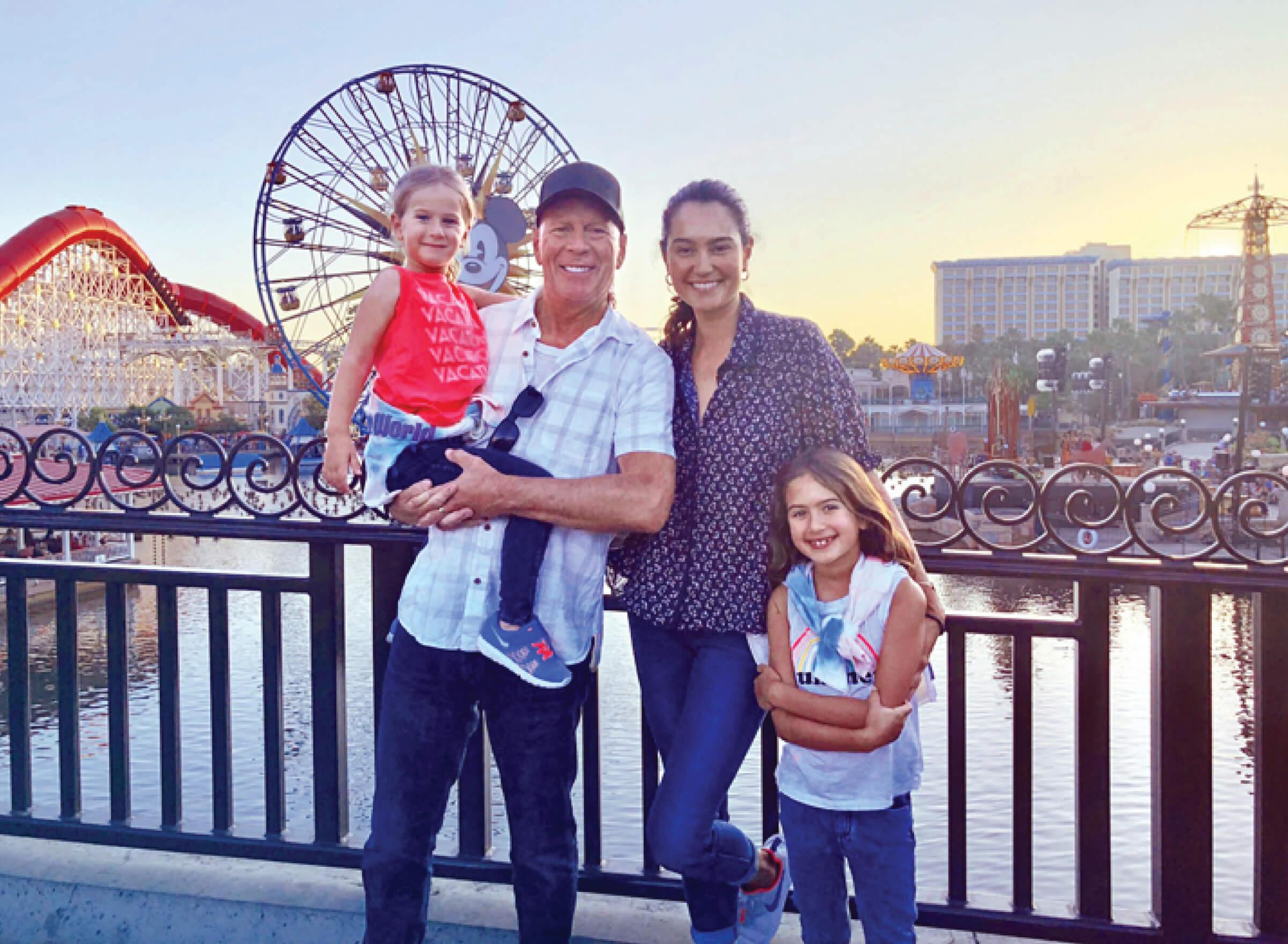 Family picture of Bruce Willis with his wife and daughters standing in front of a ferris wheel at disneyland