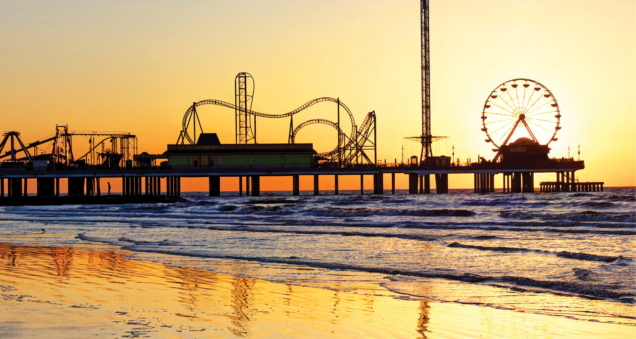 A sunset picture of the Galveston Beach, Texas showcasing the rides of the amusement park on the beach