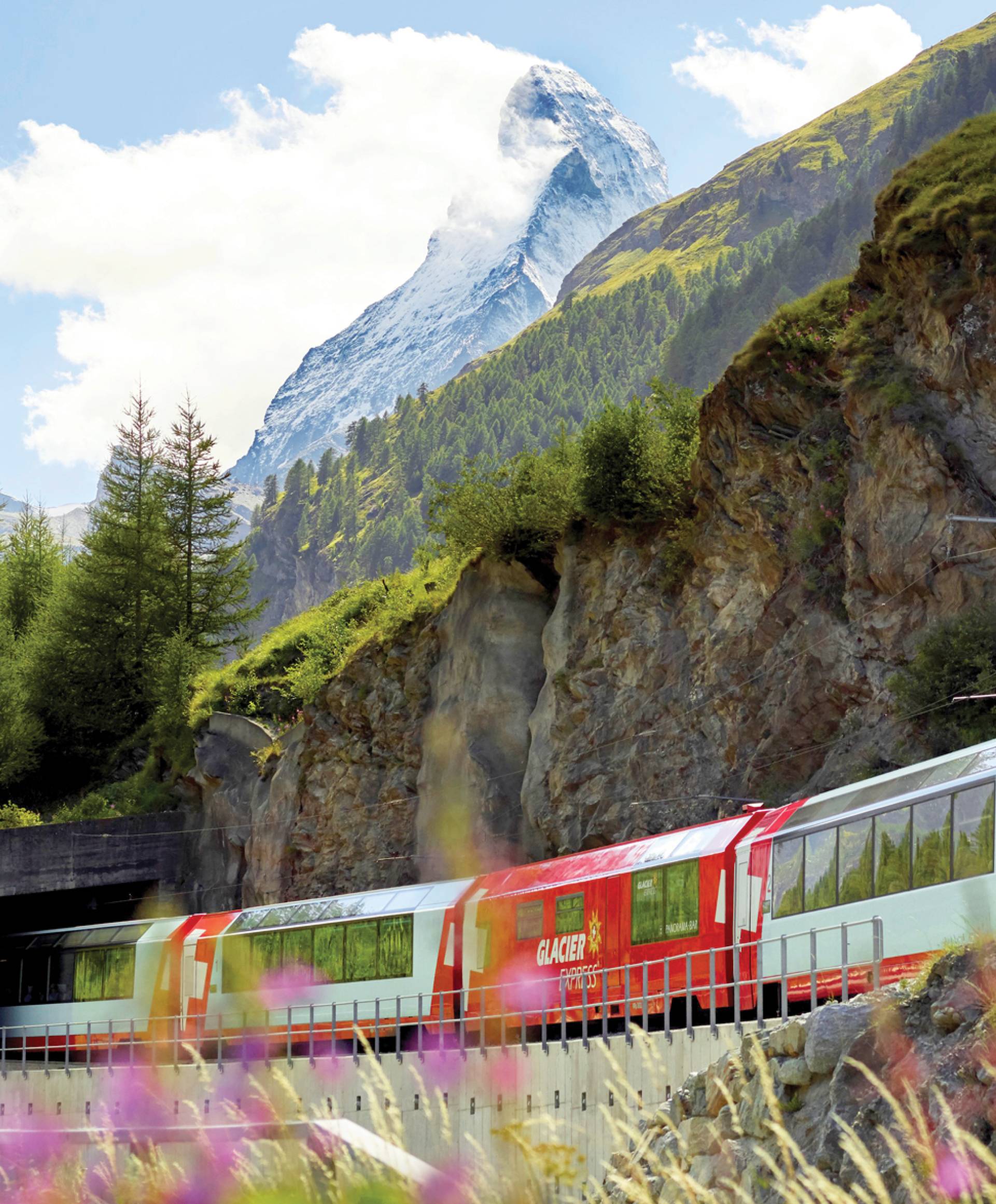 Photograph of a bright red train, the Glacier express running through the beautiful Alpine landscape of Switzerland