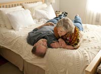 Ageless Love-AARP-Michael Downs, wife Sheri Venema smile on bed at home.