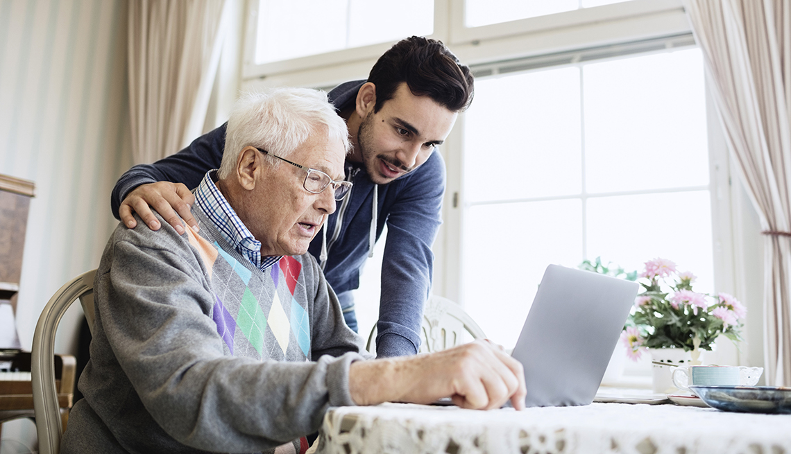 Hombre mayor frente a un computador portátil y hombre joven a su lado