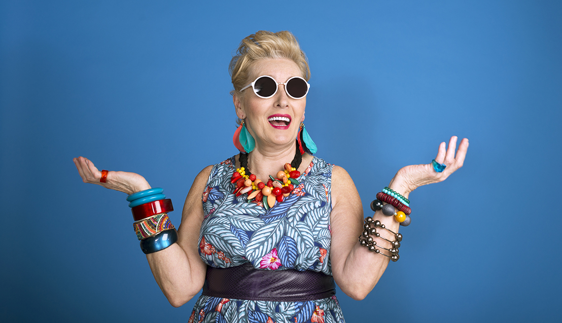 Blue background with creative, colorful mature woman standing in front of it, wearing sunglasses 