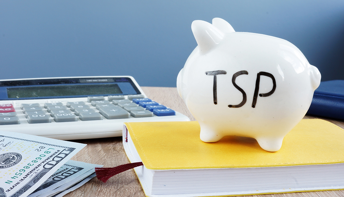 Thrift savings plan TSP written on a piggy bank on a desk with book, cash and calculator