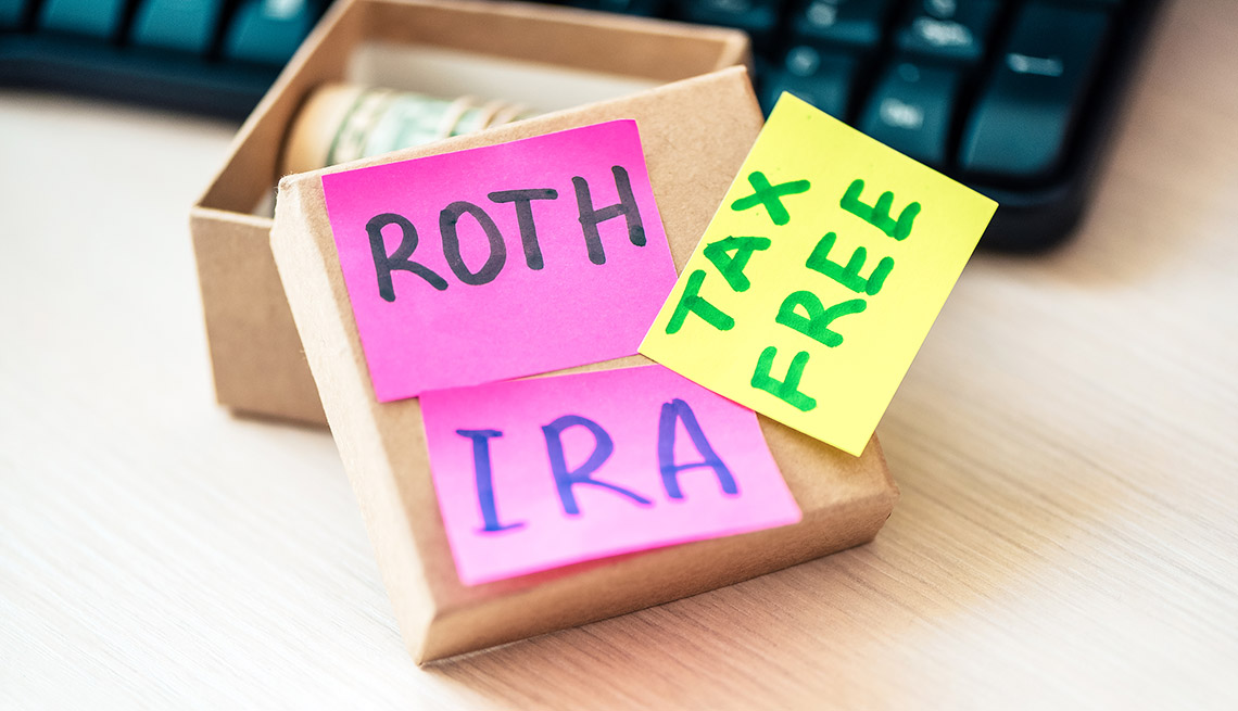 Papeles de notas que dicen ROTH IRA y libre de impuestos al lado de una caja con dólares enrollados.