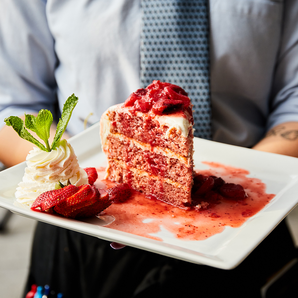 a waiter holds a large plate containing a slice of strawberry cake 