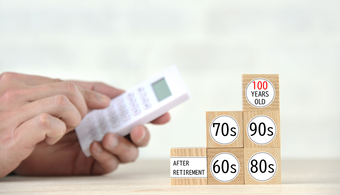 Close up of hands using a calculator next to a stack of wooden blocks marked with decades of age from "after retirement" to "100 years old".