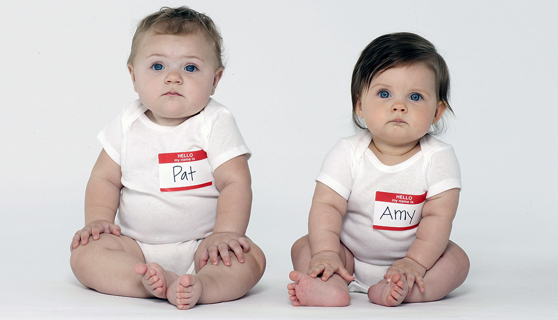 Two babies sit facing camera wearing stick on name tags on white tshirts that say Pat and Amy