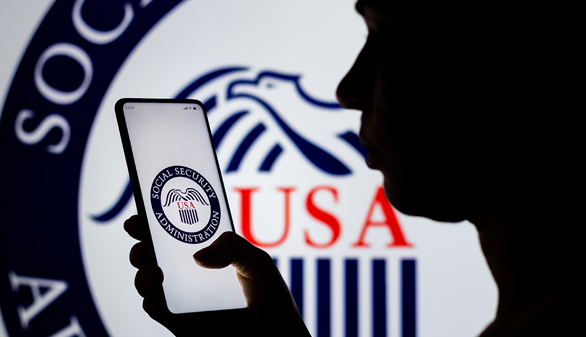 A woman's silhouette holds a smartphone with the United States Social Security Administration logo displayed on the screen and in the background.