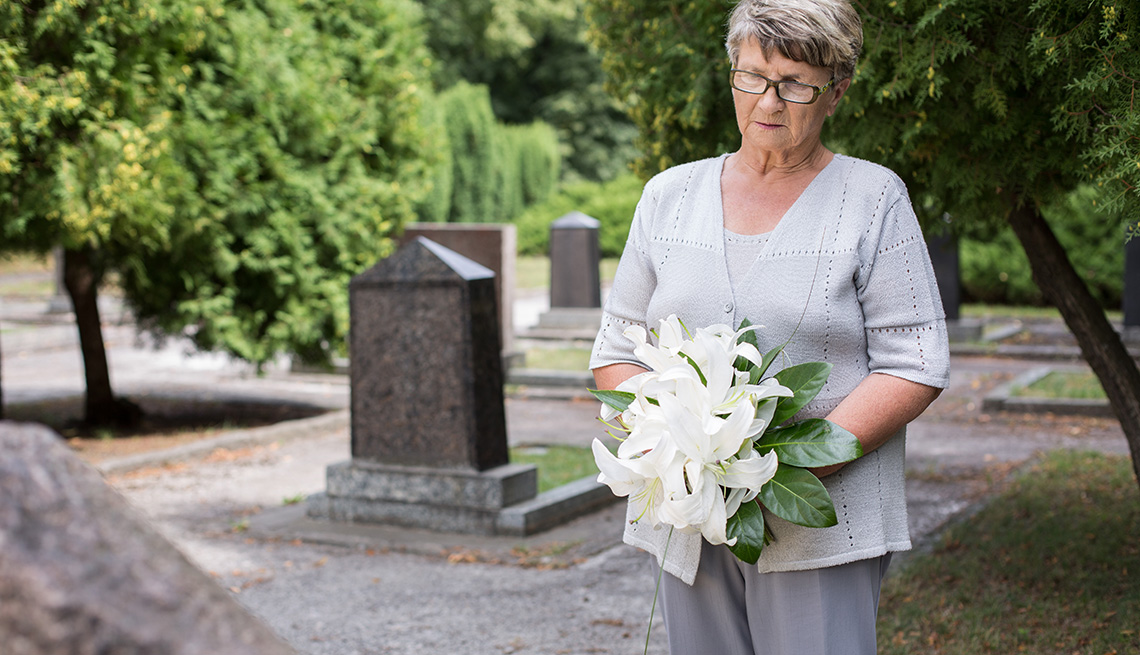 Older woman holding lilies while mournfully looking at her partner's grave