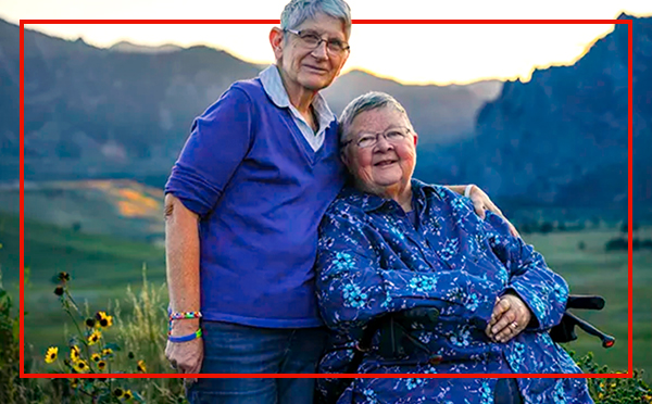 Two older women, one sitting, one standing, enjoying a beautiful mountain landscape
