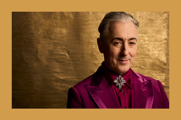Photo of Alan Cumming looking dashing in a suit with a gold background and photo border.