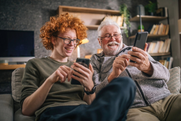 Grandson and Grandfather sitting on the couch laughing with their phones. 