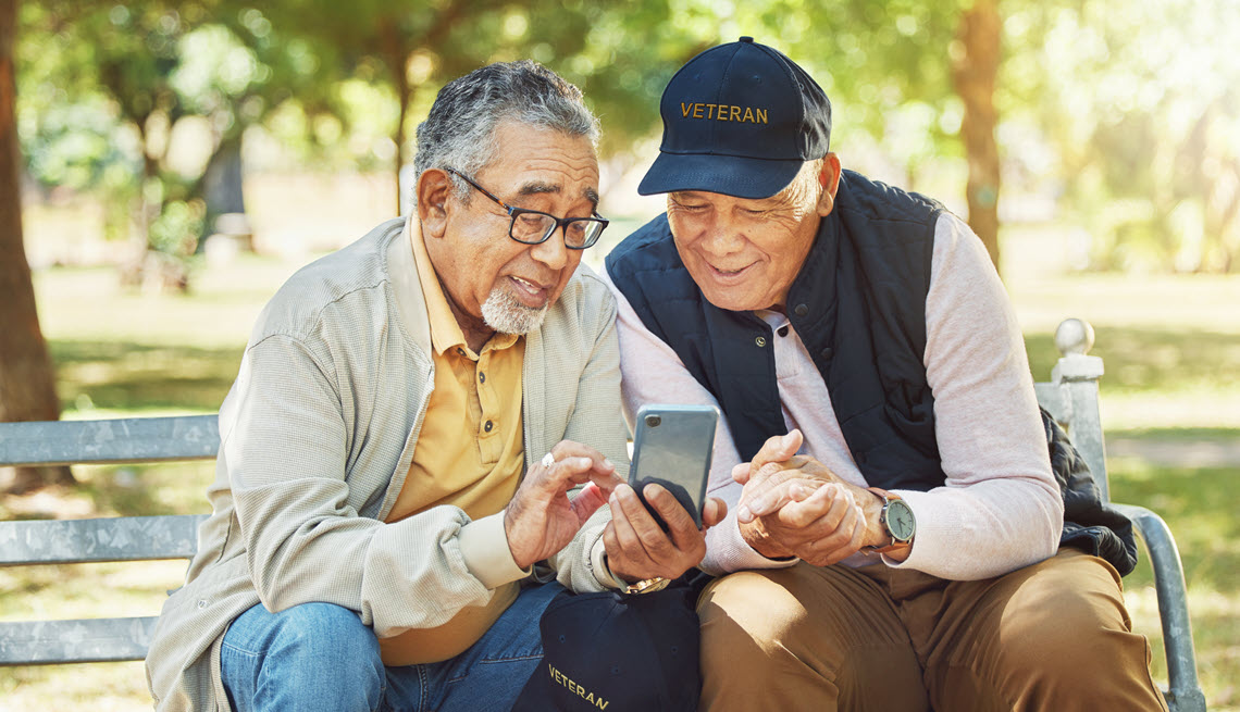 Two veterans on a bench looking at a phone