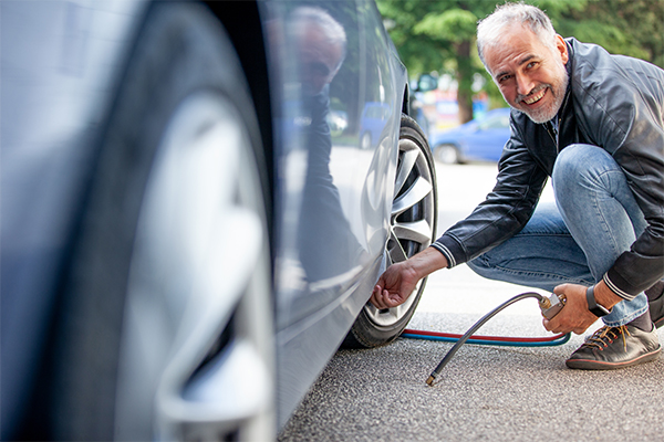 Man with grey hear wearing a leather jacket bending over to put air in his car tires