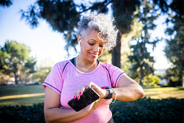 Mature woman wearing workout clothes walking outdoors looking at her fitness tracker 