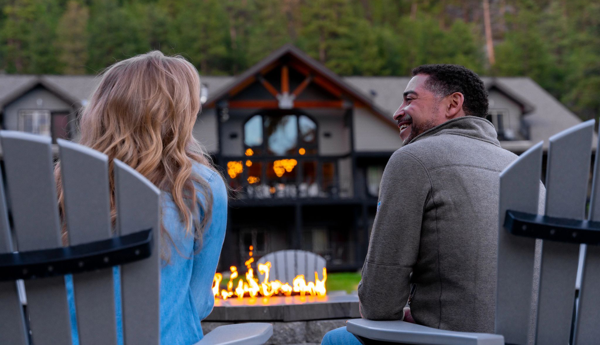 Couple sitting in Adirondack chairs by an outdoor fire pit at a hotel in the woods