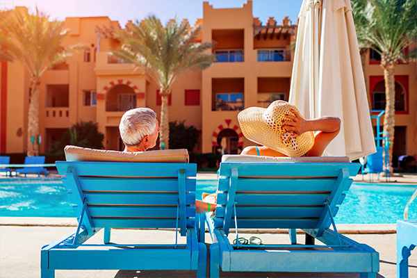 Couple relaxing in blue chairs by the pool at their resort with palm trees in the background