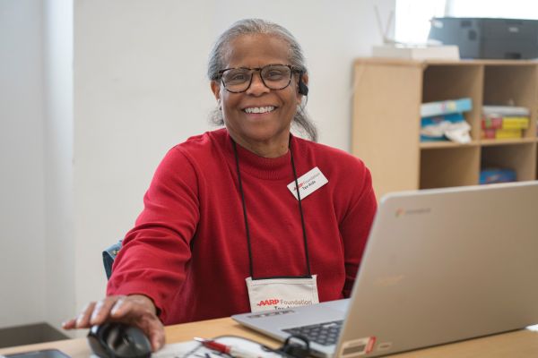 woman sitting at computer wearing red shirt with AARP Foundation tax aide nametag on