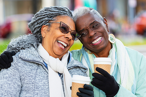 women drinking coffee outside in winter and smiling
